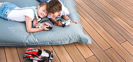 Holzfarbene Terrasse mit zwei Kindern auf einem Kissen und einem Spielzeugauto